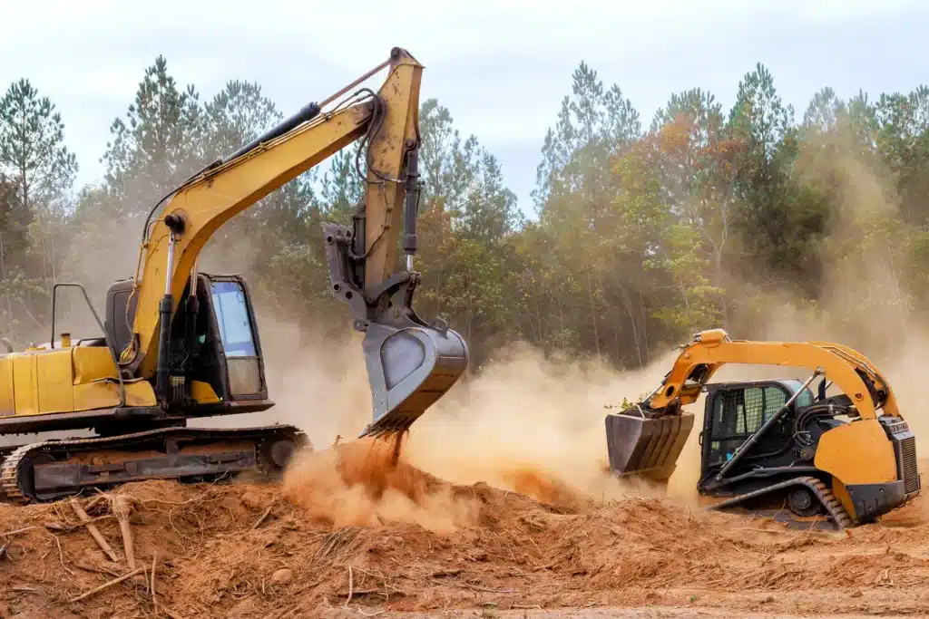 Excavator and skid steer performing land clearing and grading work on a construction site